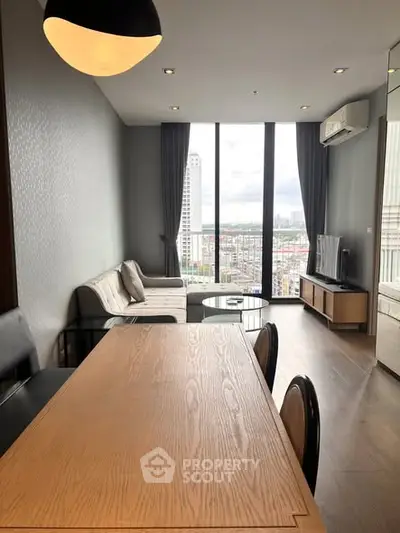 Modern living room with large windows offering city views, featuring stylish furniture and sleek design.