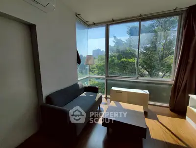 Bright living room with large windows and modern furniture overlooking lush greenery.