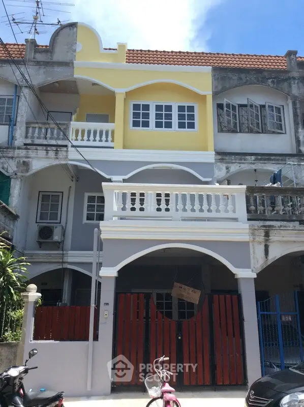 Charming two-story townhouse with vibrant yellow facade and balcony, perfect for urban living.