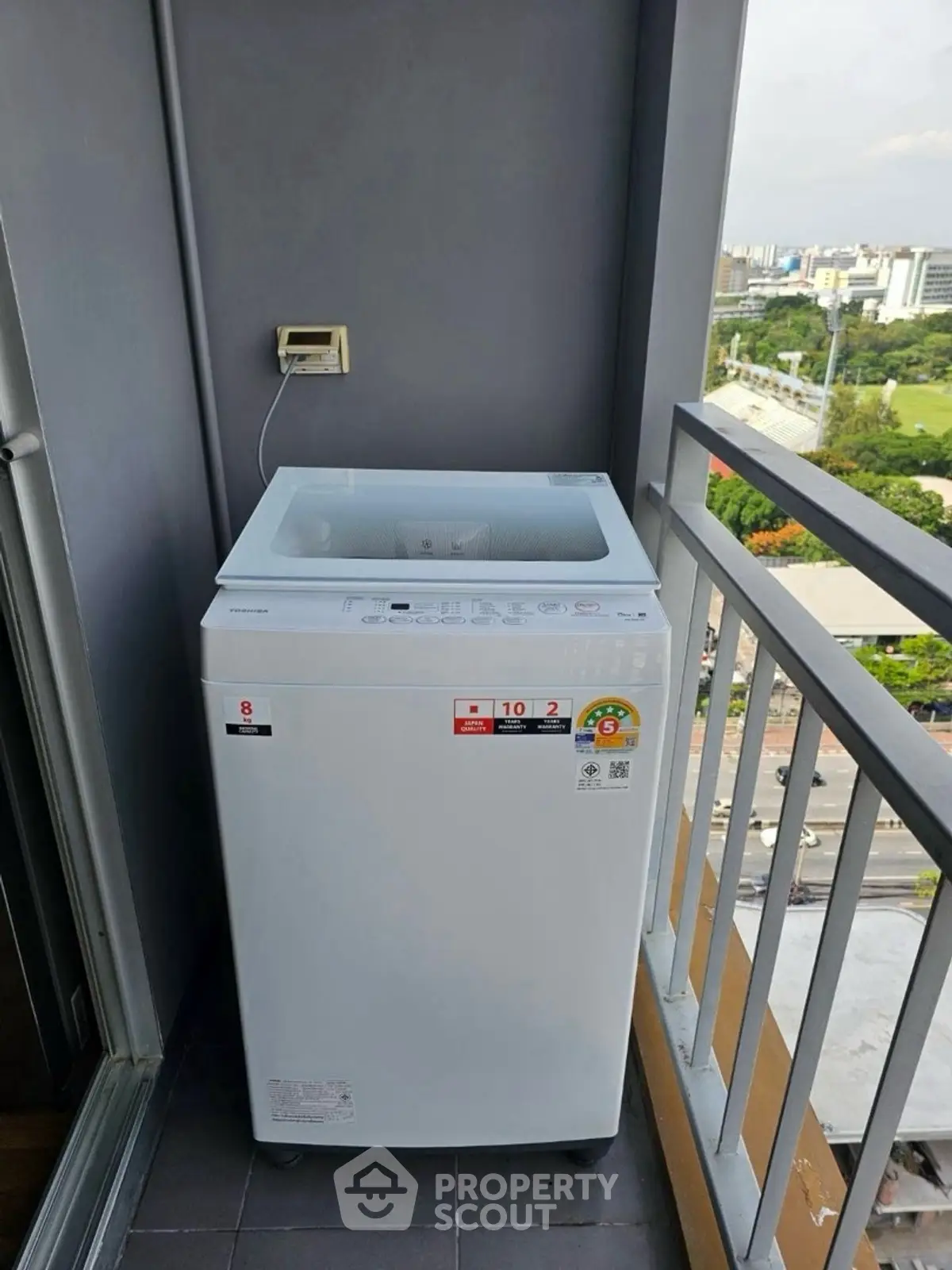 Compact washing machine on a high-rise balcony with city view.