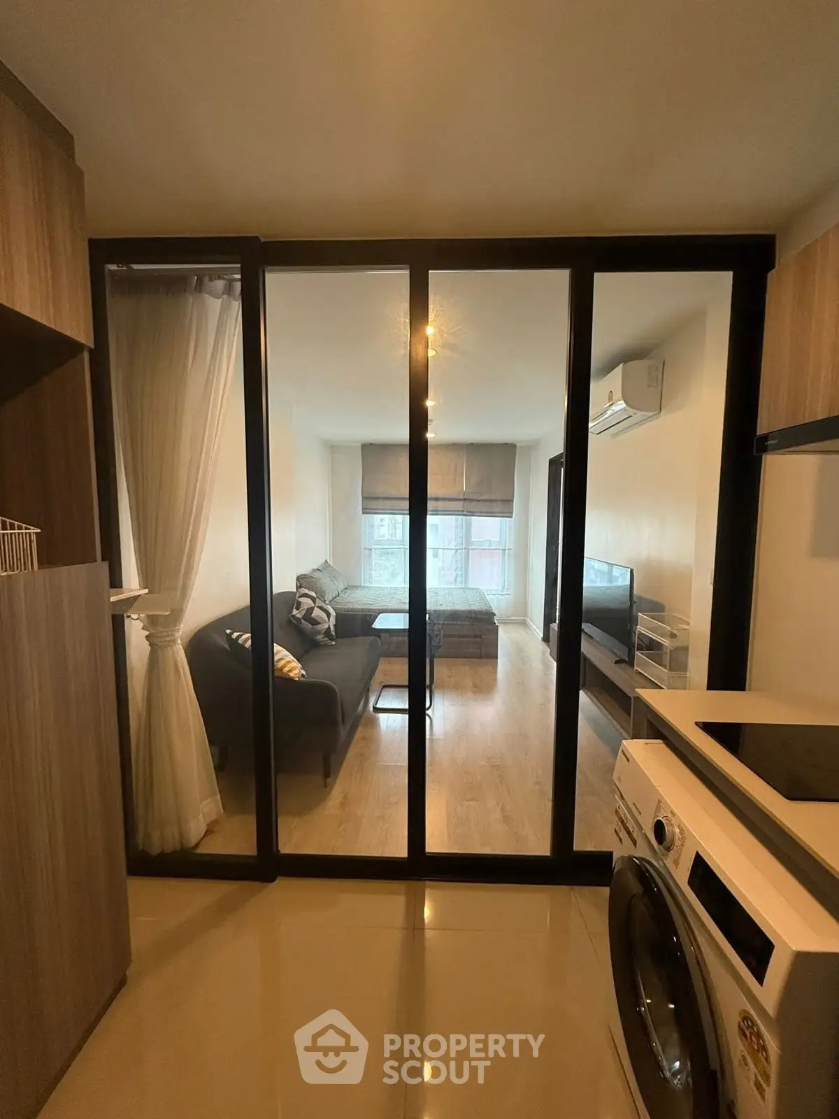 Modern apartment with glass partition, cozy living area, and in-unit washing machine.