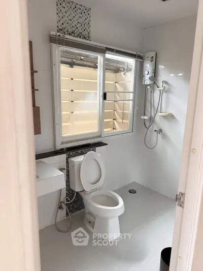 Modern bathroom with shower and toilet, featuring sleek white tiles and natural light.