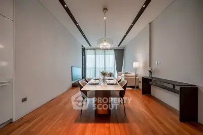 Elegant modern living room with dining area and chandelier, featuring sleek wooden flooring.