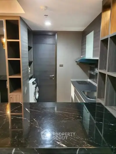 Modern kitchen with sleek black marble countertop and built-in washing machine.