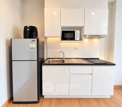 Modern compact kitchen with sleek cabinets, fridge, and microwave in a stylish apartment.
