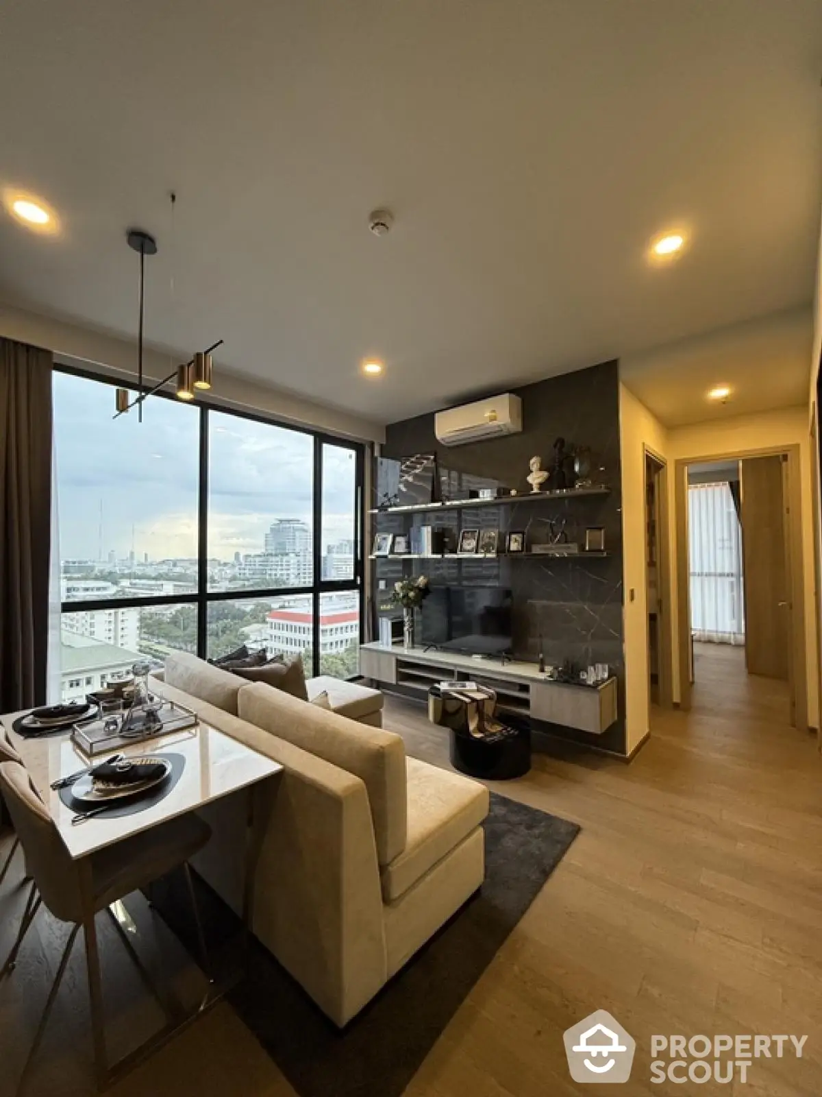 Modern living room with city view, stylish decor, and open dining area in high-rise apartment.