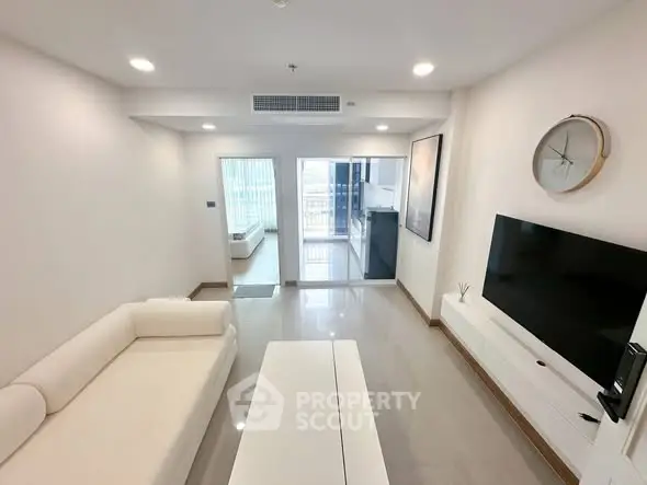Modern living room with sleek white furniture and wall-mounted TV, leading to a bright balcony.
