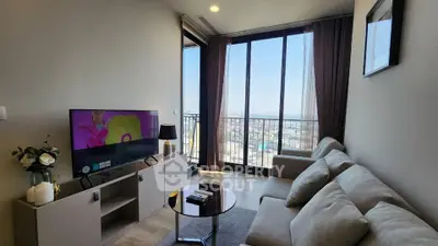 Modern living room with large windows and city view, featuring cozy sofa and entertainment center.