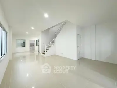 Spacious modern living room with sleek tile flooring and staircase in a bright open layout.