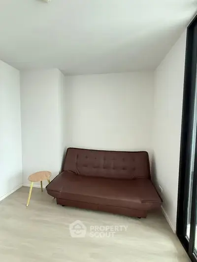 Minimalist living room with brown sofa and small wooden side table, bright and airy space.