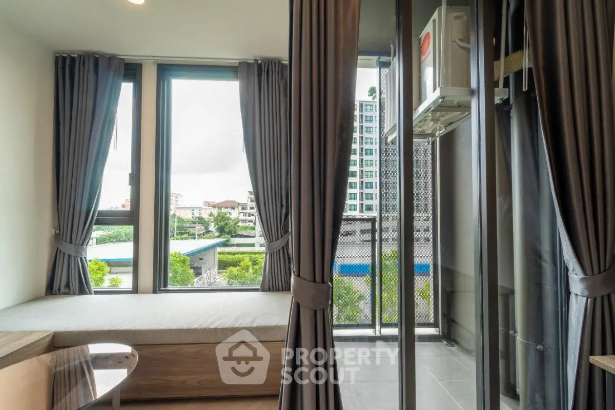 Modern apartment with large windows and city view, featuring elegant curtains and cozy seating area.