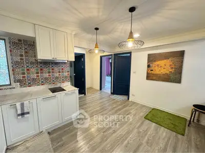Charming open-layout kitchen with modern lighting and colorful backsplash tiles.