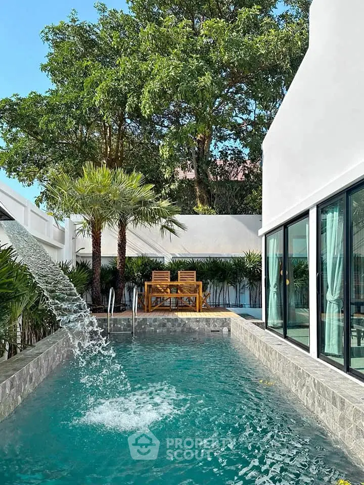 Luxurious private pool with waterfall feature in modern villa surrounded by lush greenery.