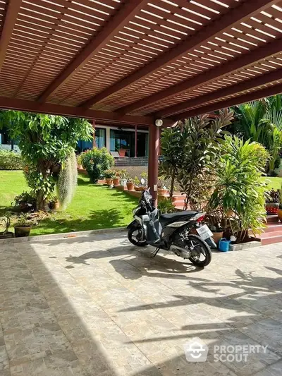 Spacious garden with covered patio and motorcycle, ideal for outdoor relaxation.