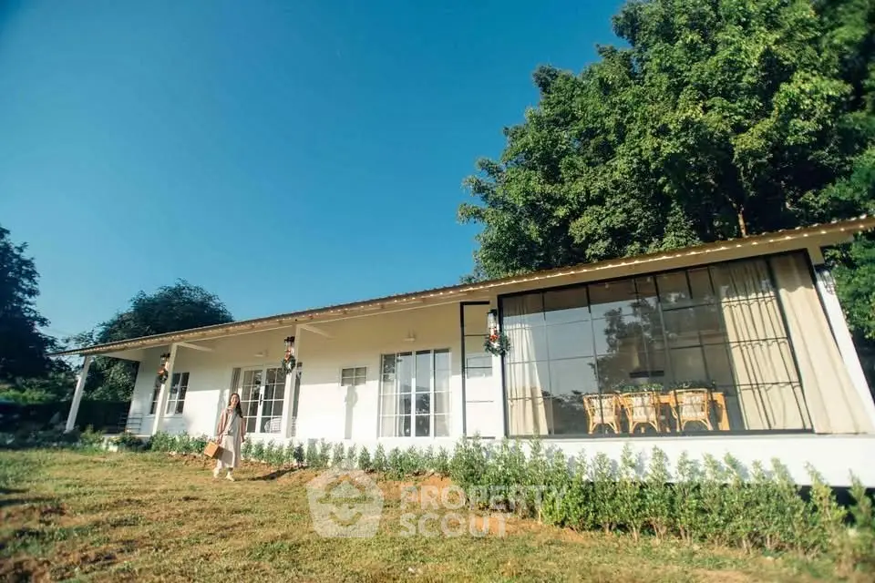 Charming single-story home with large windows and lush greenery, perfect for serene living.