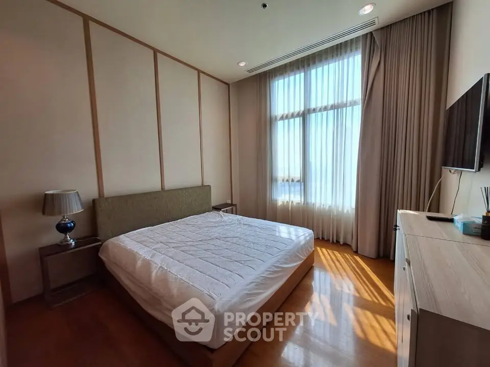 Spacious bedroom with large window and modern furnishings in a luxury apartment.