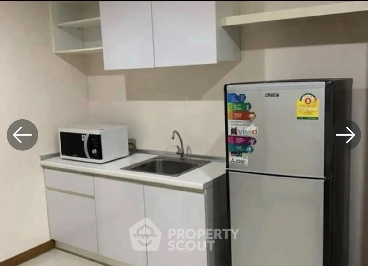 Modern kitchen with sleek cabinets, microwave, and stainless steel fridge.