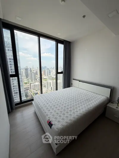 Modern bedroom with stunning city view from floor-to-ceiling windows in high-rise apartment.