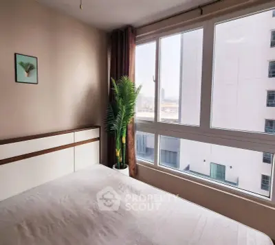 Bright bedroom with large window and city view, featuring modern decor and a potted plant.