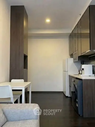 Modern kitchen with sleek cabinets, washing machine, and dining area in a cozy apartment.
