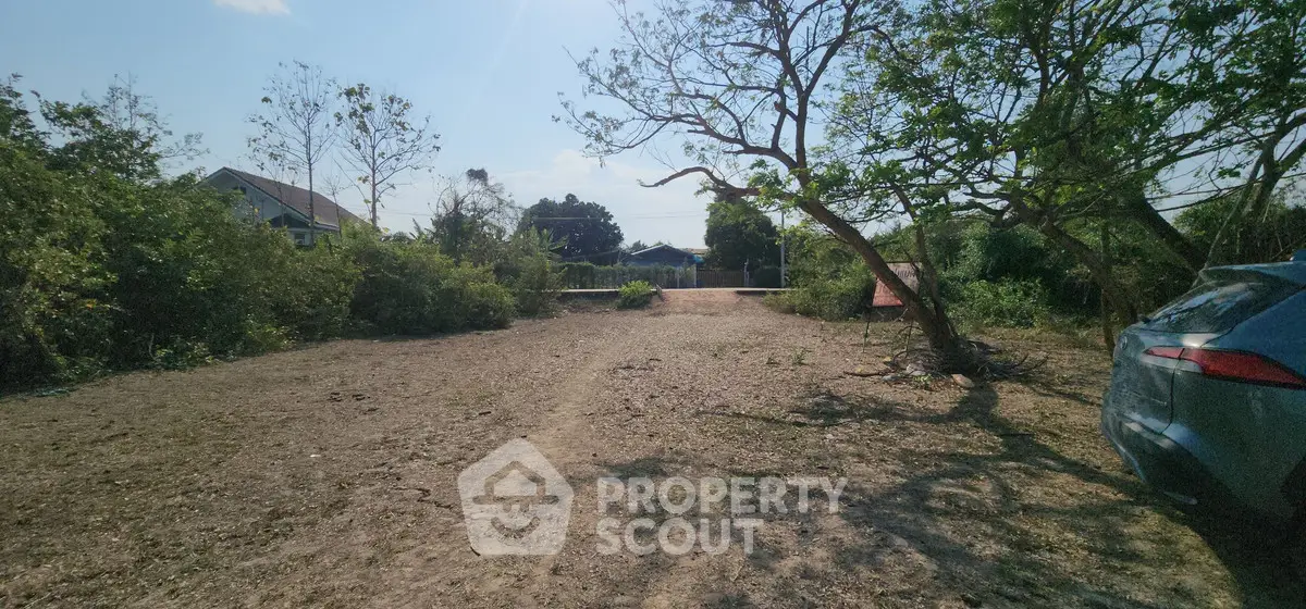 Spacious vacant land with potential for development, surrounded by greenery and a clear sky.