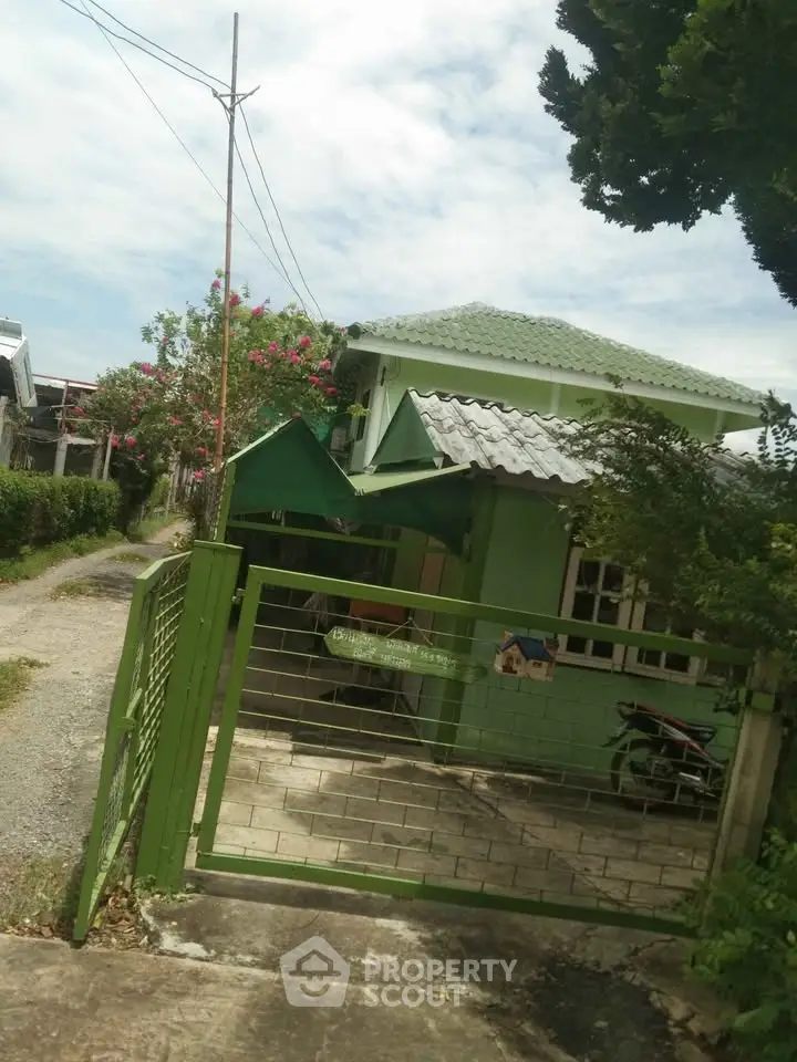 Charming green house with gated entrance and lush garden in a serene neighborhood.