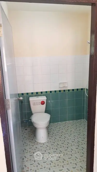 Modern bathroom with green tiles and white fixtures, featuring a sleek toilet and tiled floor.