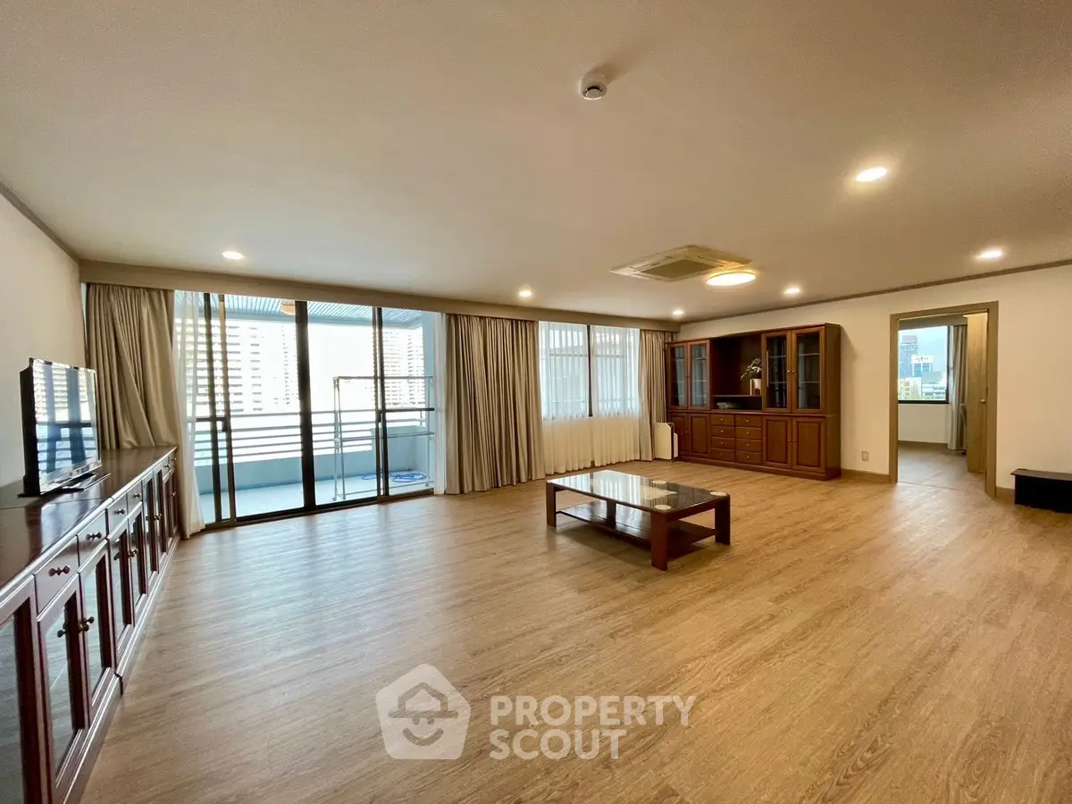 Spacious living room with wooden flooring and large windows offering city views.