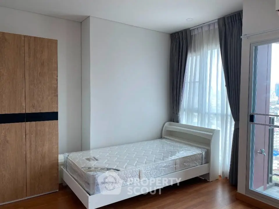 Modern bedroom with large window and wooden wardrobe in a high-rise apartment.