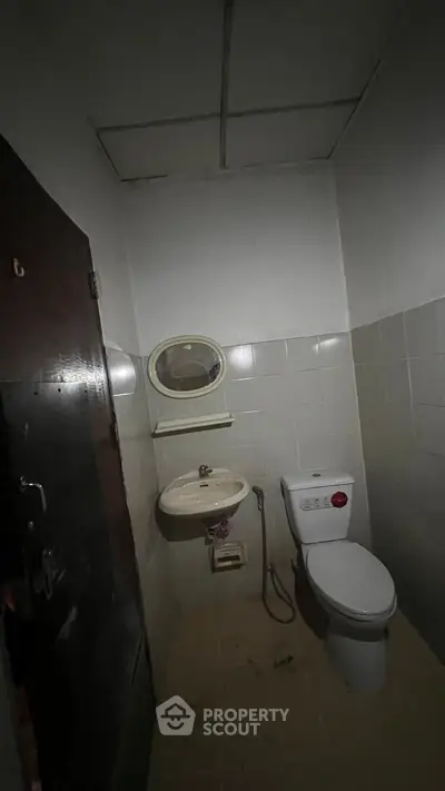 Compact bathroom with basic fixtures and tiled walls, featuring a toilet and sink under dim lighting.