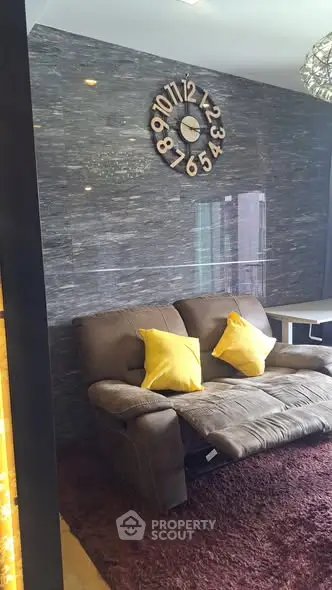 Modern living room with stylish wall clock and cozy brown sofa accented by yellow pillows.