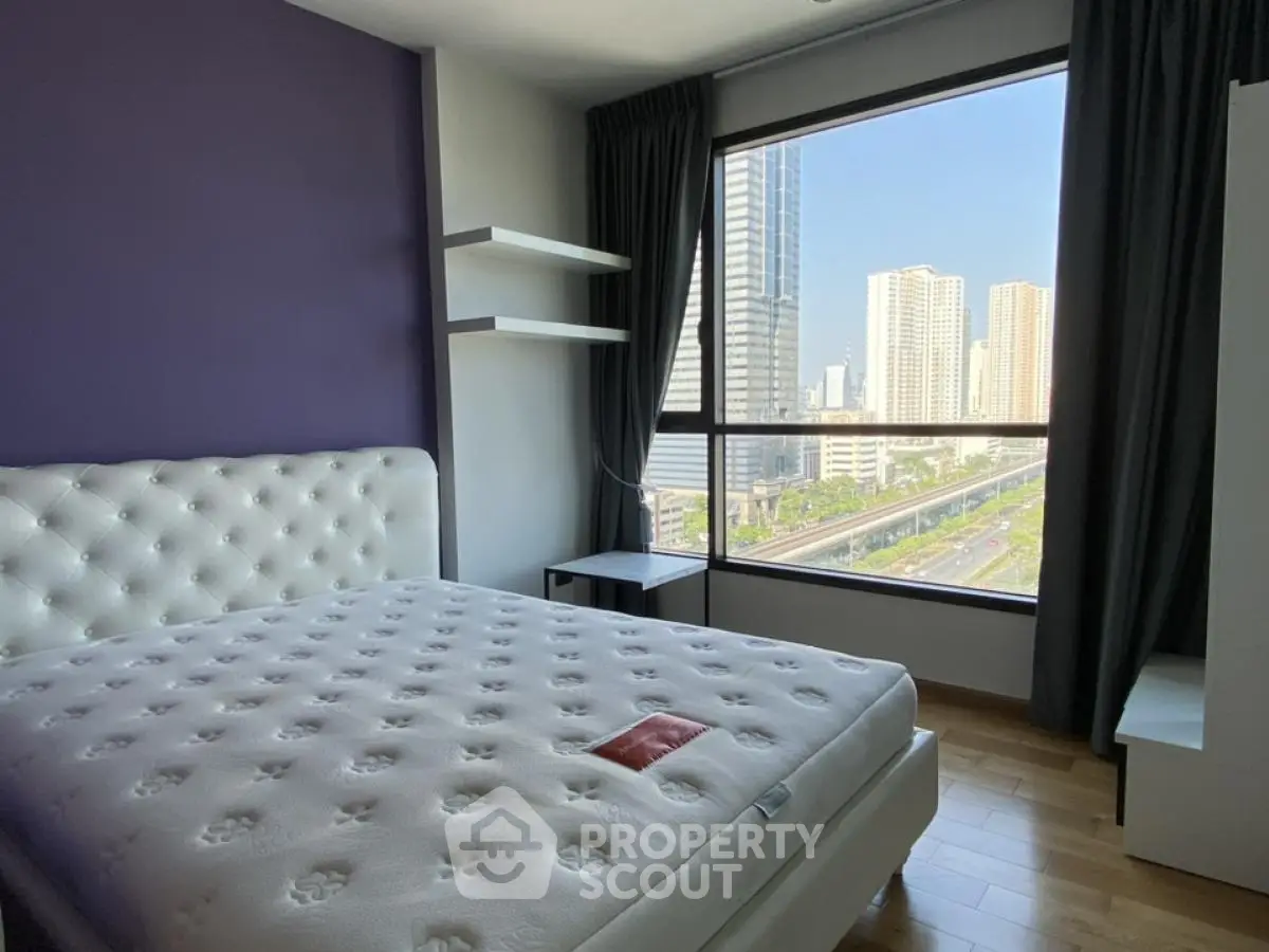 Modern bedroom with large window offering stunning city view in high-rise apartment.