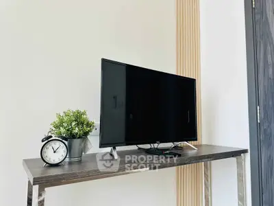 Modern interior with sleek TV on stylish console table, complemented by a decorative plant and clock.