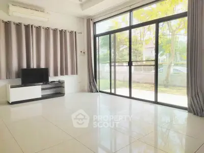 Spacious living room with large windows and modern decor, offering abundant natural light and garden view.