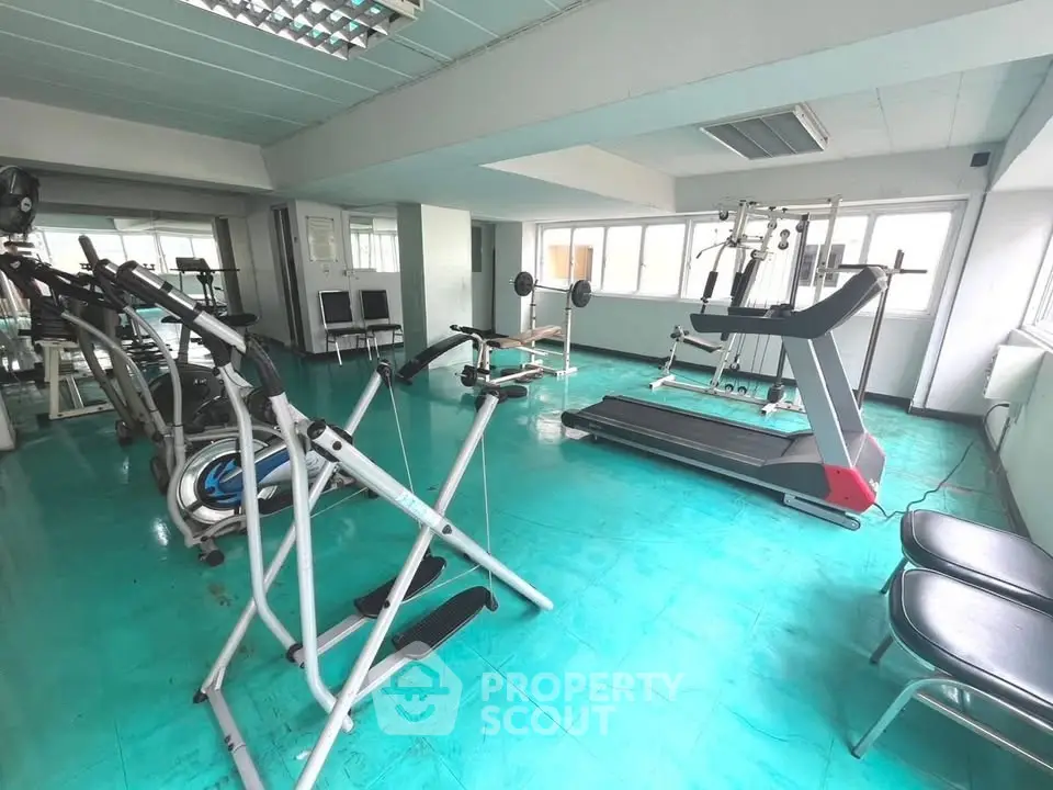 Spacious gym with modern equipment and bright turquoise flooring in a residential building.