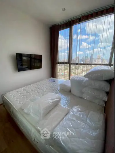 Modern bedroom with large windows offering stunning city views and a wall-mounted TV.