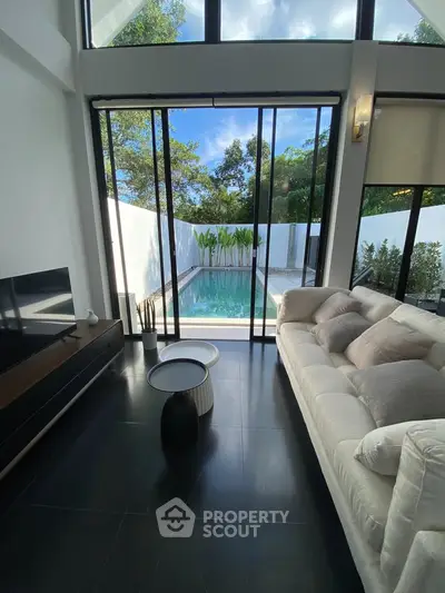 Luxurious living room with pool view, modern furniture, and floor-to-ceiling windows in a serene setting.