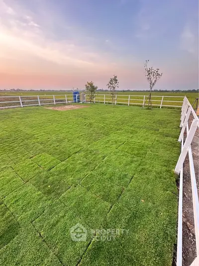Expansive green lawn with white fencing and scenic countryside view at sunset.