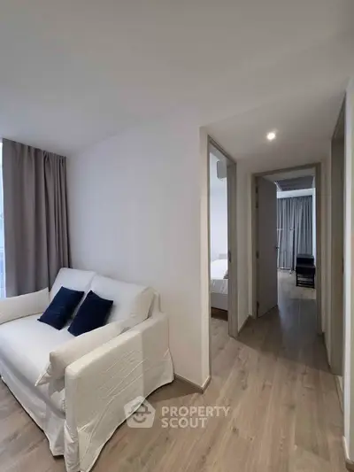 Modern apartment interior with cozy living area and hallway leading to bedroom, featuring sleek wooden flooring.