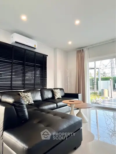 Modern living room with black leather sofa and large windows offering natural light.