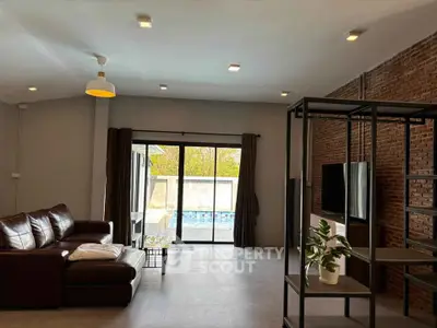 Spacious living room with modern decor and pool view, featuring a leather sofa and large windows.