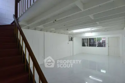 Spacious open-plan interior with white walls and tiled flooring, featuring a wooden staircase.