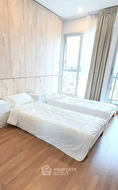 Bright and spacious bedroom with twin beds and large window offering city views.