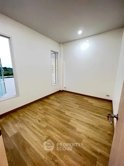 Spacious empty room with wooden flooring and large windows, perfect for customization.