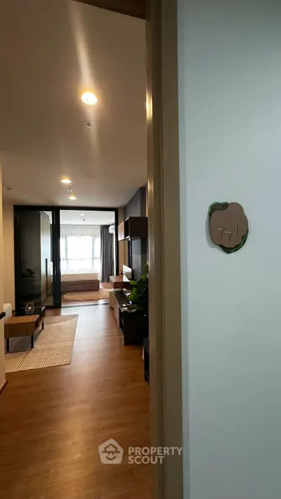 Modern apartment entrance leading to a stylish living room with wooden flooring and natural light.