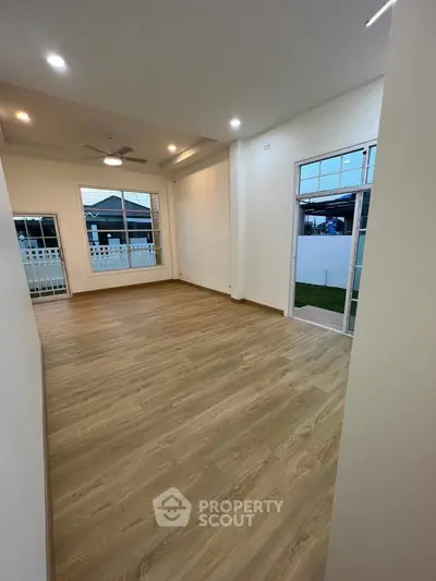 Spacious living room with wooden flooring and large windows for natural light.