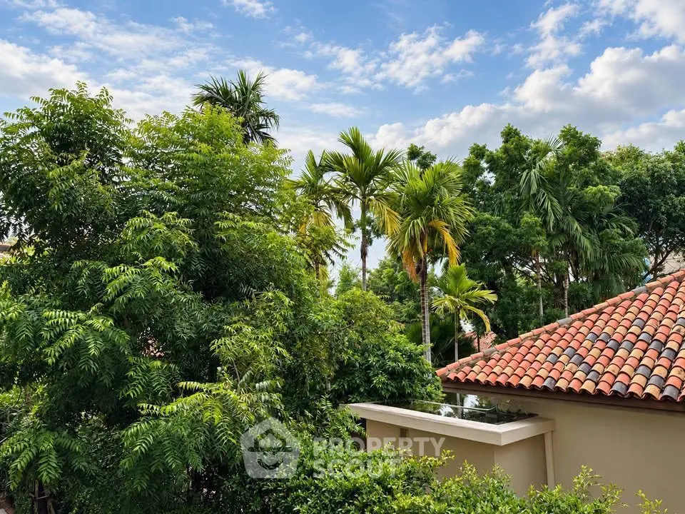 Lush tropical garden view with red-tiled roof under a vibrant blue sky.
