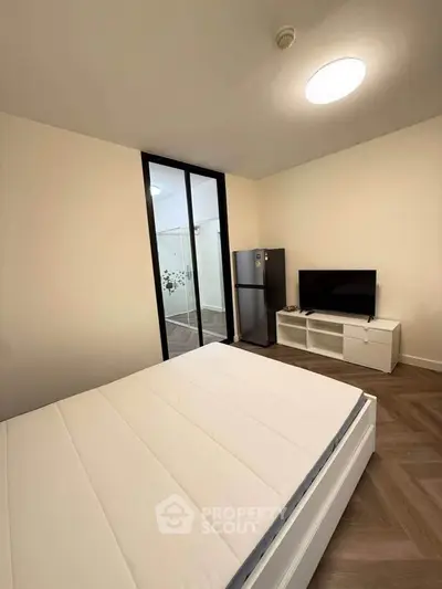 Modern bedroom with minimalist design, featuring a bed, TV, and compact fridge for convenience.