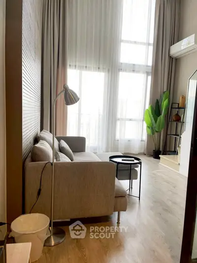 Modern living room with high ceilings and large windows, featuring a cozy sofa and stylish decor.