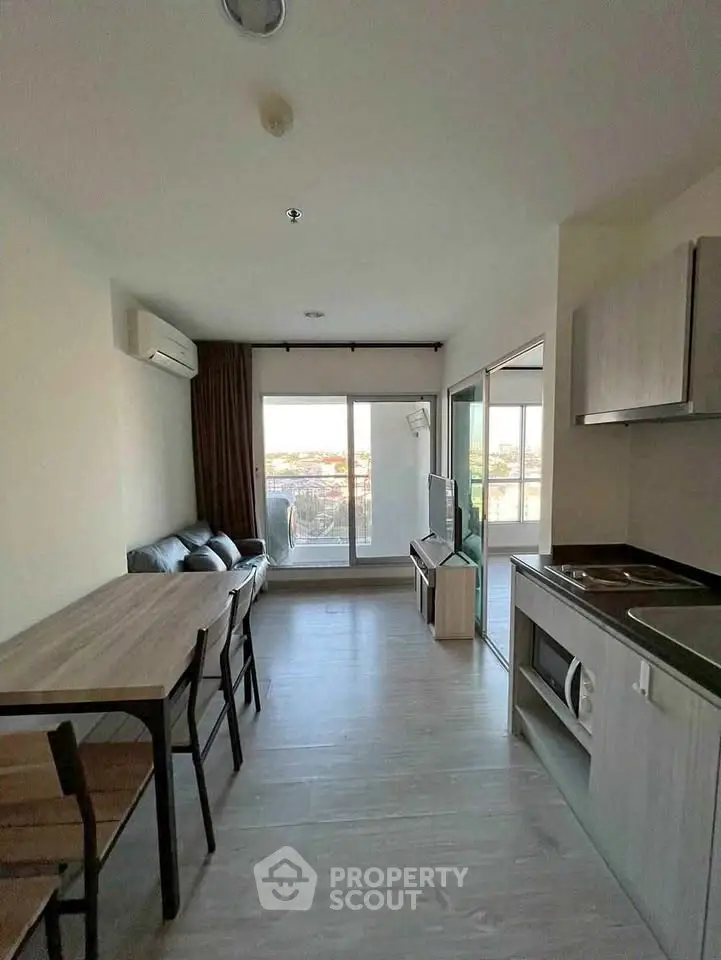 Modern living room with open kitchen and balcony view, featuring sleek furniture and natural light.